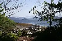 A pebble beach along the water with mountains visible in the far distance