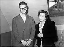 Black and white photograph of a handcuffed man with a woman at his side.