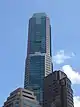 Ground-level view of 70-storey building. The exterior has a reddish hue with dark windows. The building tapers slightly at two points.