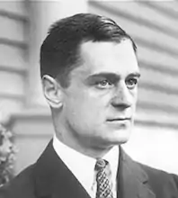 a white man with a short haircut looking to the right, he is wearing a suit and tie