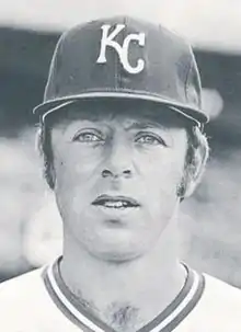 A man in a light baseball jersey and dark cap