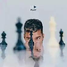 A man looks into a table with different chess pieces placed on it. A pause and play icon is seen above the man's head, with the play icon (and the album's title) labeled in blue colors.