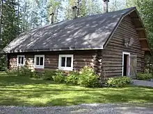 The stable, a one-story log structure painted brown with a shingled roof, is one of the outbuildings on the property