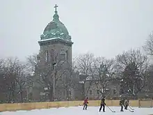 Children skating on an ice outdoor ice rink in a city park with a large church in the distance