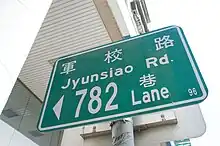 A green street sign for 軍校路, romanized as Jyunsiao Rd.