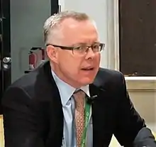 Photograph of Rob Monster from the shoulders up, wearing a suit and tie and speaking