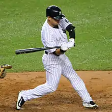 A baseball player in a white baseball uniform and a navy blue helmet swinging at a pitch