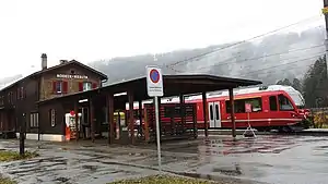 Two-story building with gabled roof next to railway line with red train