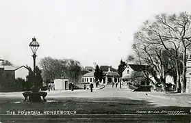 A street scene of Main Road Rondebosch, Cape Town around the turn of the 20th century.  The recently installed Rondebosch Fountain can be seen to the left in the foreground.