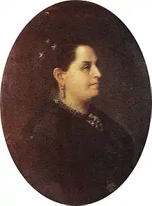 Portrait of a middle-aged woman with tan skin, dark eyes, and dark hair dressed in an updo with jeweled ornaments at the crown, she is wearing a dark dress, drop earrings, and an necklace