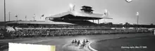 A black and white photograph depicting a race at Rosecroft. Six horses are making a turn, and 6,000 people are watching.