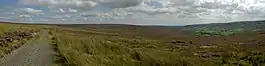 A view of a moorland path on the left, with a deep u-shaped green valley on the right