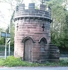 Photograph of a short round brick tower in a central reservation of an English road, the remnants of the abbey's gatehouse