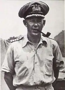 Outdoor half-length portrait of man in light-coloured military uniform with peaked cap, smoking a pipe