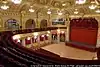 Picture taken from the grand circle of a theatre auditorium with gold decorative features with a small Centre stage and red curtain