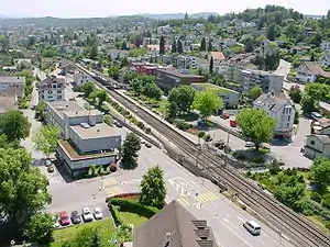 Aerial view of a town; the station is at center next to a double-track railway line