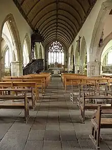 Photo of a church interior, showing the nave covered by a panelled roof frame, arcades on the sides and the apse pierced by a large stained glass window.