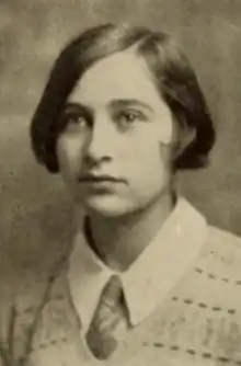 A young white woman with straight bobbed hair, side-parted, wearing a collared shirt and tie and a knitted v-neck sweater