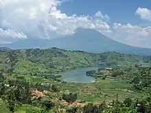 Photograph of a lake with one of the Virunga Mountains behind, partially in cloud