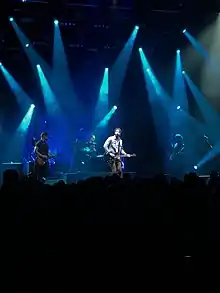 A picture of singer Ryan Hurd strumming a guitar and singing while on a stage.