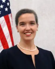 Oudkirk smiling, standing in front of an American flag