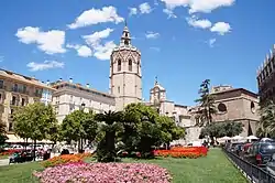 a view of flower beds in full bloom and over trees the top of the cathedral and the Miguelete Tower