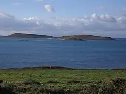 Looking from the grassy shore of Tresco, across the calm water, to the low twin hills of Samson