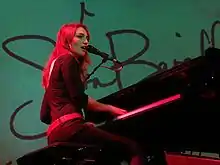 An image of an woman playing a grand piano against a teal background.