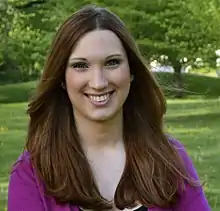 A portrait of Sarah McBride taken in 2016. She is wearing a fuschia-colored sweater and is smiling.