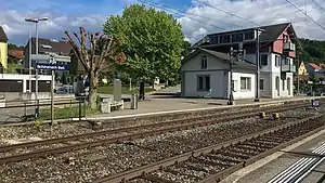 Three-story building with gabled roof next to double-track railway line with side platforms