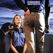 A girl kneeling and a Doberman Pinscher sitting in front of a man with his hand in the rear pocket of his jeans.