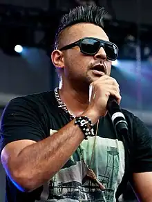 alt=Sean Paul singing wearing a black shirt with a green design
Calvin Harris performing in a blue shirt with green lights behind him.