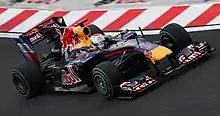 A navy-and-yellow single-seater racing car is driven around a tarmac course.