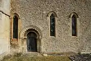 Part of the south wall of the chancel of St Faith's church, showing the 12th-century Norman priest's door and 14th-century Decorated Gothic windows