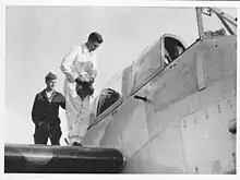 A pilot stands on the wing of an aircraft as he prepares to enter the cockpit