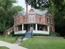 A two-story brick house with a raised wraparound porch