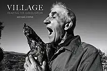 Front cover of Village: Hearing the Grass Grow. Includes the title and author name over an image of an Italian farmer singing to one of his hens.