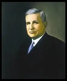 A color portrait of a gray-haired man in his early sixties wearing a suit