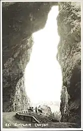 black-and-white postcard image depicting a road in a canyon with 1 vehicle