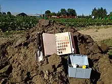 Soil Munsell color book, hand trowel, and equipment kit located on a pile of soil in British Columbia, Canada