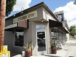 Photograph of the exterior of a corner building and adjacent sidewalk with outdoor seating