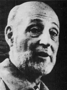 A black-and-white image of a middle-aged bald man who is speaking