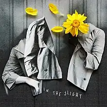 On dark wood, black-and-white images of a woman in a coat are cut out and separated by a yellow sunflower. Three of its petals have fallen onto the paper. At the bottom, "In the Slight" is hand-written.