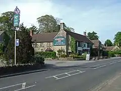 Building with pub sign saying the Sparkford Inn with car park and road in the foreground.