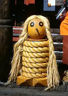 Wooden doll with rope coiled around it in a spiral.