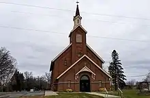 dark red brick church with a tall steeple. St. Edward's cemetery is visible in the far background