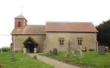 Side view of a building, which has a small tower on the left side: tombstones lie in rows on plots in front.