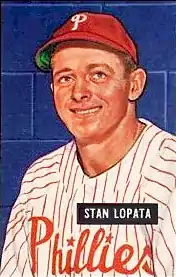 A baseball card image of a smiling man wearing a white baseball uniform with red pinstripes and a red baseball cap with a white "P" on the front