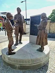 The artwork depicts Boole at a blackboard teaching a boy and girl  that the symbols of logic are subject to a special law.