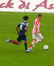 Andrea De Falco, playing football for Tre Fiori. In this image, he is about to tackle an opposition player in front of the advertising boards